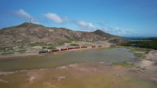 Line of transport semi trucks parked on sandy slope next to polluted green pond