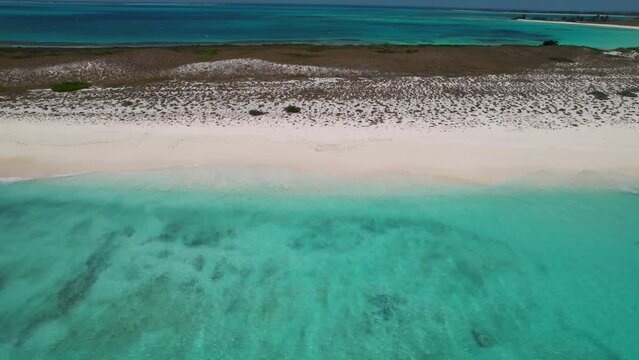 Fast aerial pullback from white sand to light blue ocean water reef and cove with grass