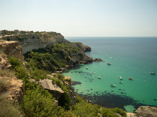 Sunlit Coastal Serenity: Aerial View of Tranquil Seascape with Tiny Sailboats, Cliffs, and Distant Figures Enjoying the Vibrant Turquoise Waters, Evoking Vacation Bliss and Joyful Escapism