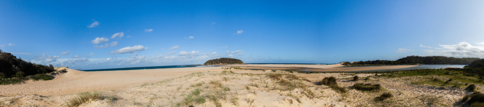 Crampton island where Tabourie Creek flows into the ocean and blue sky over sand dunes