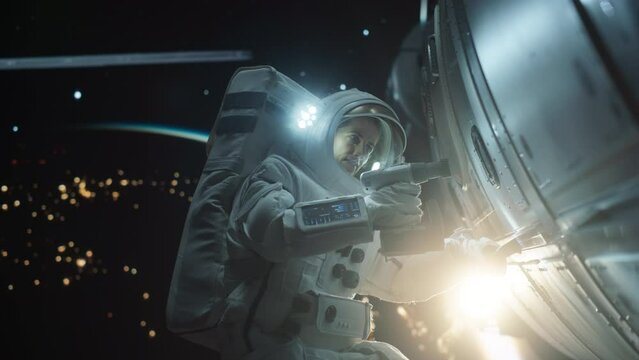 Female Space Technician Mending a Panel on an International Space Station with an Automatic Screw Gun. Fearless Astronaut Working in Outer Space with Gorgeous Blue Planet in the Background