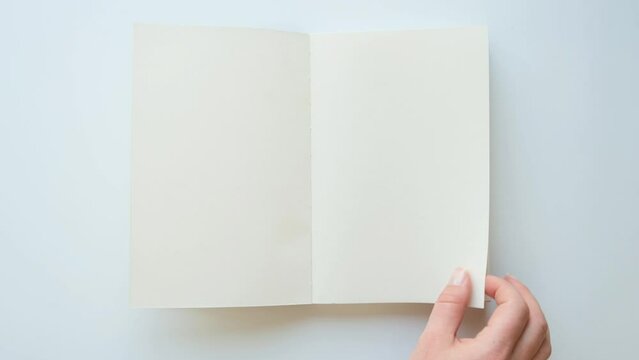 Female hands turns pages of an empty book, top view. 4K video on white background