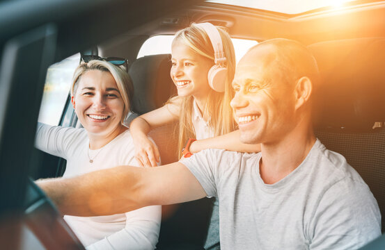 Happy young couple with daughter inside the modern car with panoramic roof during auto trop. They are smiling, laughing during road trip. Family values, traveling concepts..