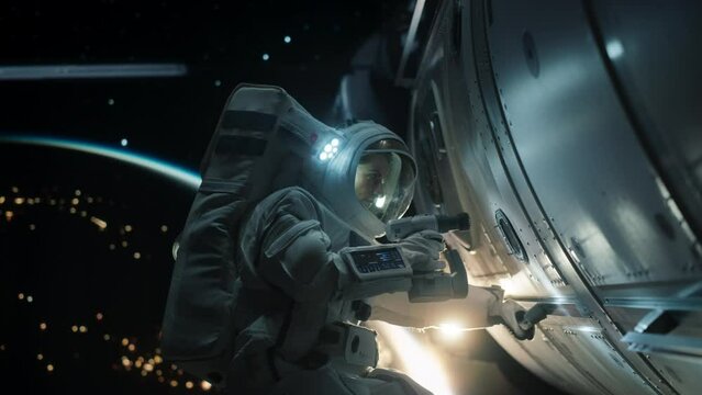 Female Space Technologist Repairing a Panel on a Spacecraft with an Automatic Screw Gun. Professional Astronaut Working in Outer Space with Dark Illuminated Planet Earth in the Background