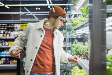 A man in the supermarket chooses fresh microgreens for a salad, healthy vegetarian food rich in...