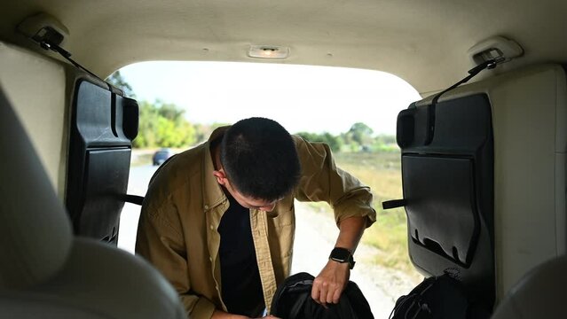 Man checking and loading his bags in the trunk of the car before starting solo journey or adventure alone
