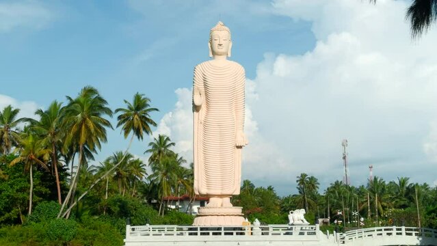 Tsunami Honganji Vihara, Hikkaduwa, Sri Lanka. Action. Beautiful white statue among green palm trees and blue cloudy sky.