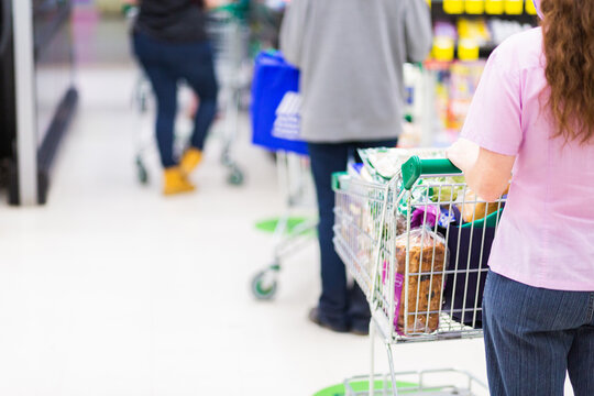 Young woman holding onto shopping trolley handle waiting in line for checkout