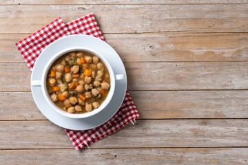 Chickpeas soup with vegetables in bowl on wooden table. Top view. Copy space