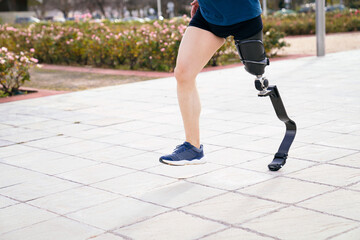 Focus on the carbon fiber sports prosthetic leg of a runner in motion, with blurred pavement and greenery in the background.