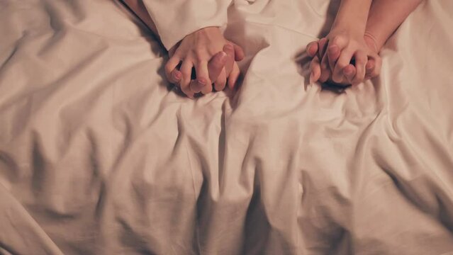 hands of woman and a man in sex on a white sheet on the bed in close-up. Couple having sex