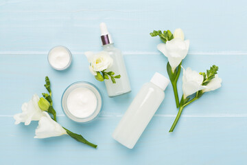 Facial cosmetic products with freesia flowers on wooden background, top view