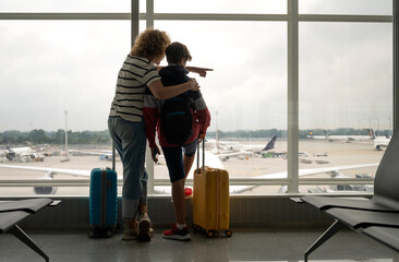 A mother and her teenage son with their suitcases watch planes at an international airport.