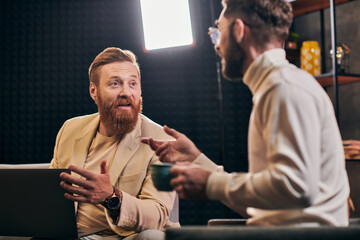 two joyful handsome men in elegant attires with coffee and laptop discussing interview questions