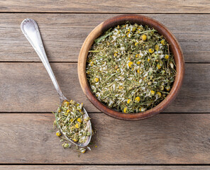 Chamomile dried tea leaves and flowers on a bowl over wooden table