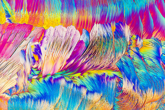 Colorful, textured layers of salicylic acid crystals form a vibrant, abstract landscape under the microscope