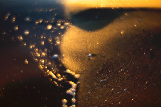 Close-up of golden droplets on a surface with a blurred shadow, evoking a sense of abstract art