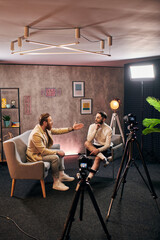 attractive elegant men in stylish clothes sitting and discussing interview questions in studio