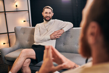 cheerful bearded men in casual outfit smiling and looking at his interviewer while sitting in studio