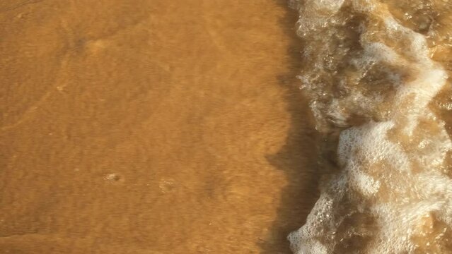 Ocean wave washes away a footprint in sand.