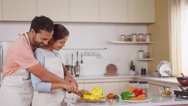 Romantic young couples cooking together by chopping vegetables at kitchen - concept of intimacy, relationship affection and companionship