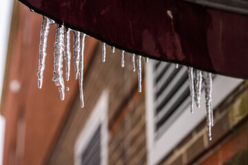 Manchester, New Hampshire, USA - Icicle hanging on a rooftop ready to melt - obrazy, fototapety, plakaty