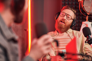 bearded interviewer with glasses talking to his blurred guest during their interview on podcast