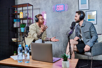 good looking interviewer and his guest with headphones in studio discussing questions, podcast