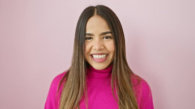 Beautiful young latin woman wearing a sweater, confidently standing and delightfully smiling. her toothy smile, full of joy and positivity, glows over the isolated pink background.