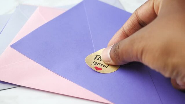 hand putting thank you sticker message on a envelope