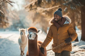 Fotobehang A bundled up woman stands with her alpaca companion, braving the winter snow as they take a peaceful walk among the trees © Sandra