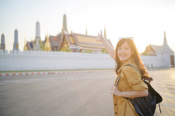 Traveler asian woman in her 30s, backpack slung over her shoulder, explores the intricate details of Wat Pra Kaew with childlike wonder. Sunlight dances on the golden rooftops.