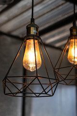 Classic style lightbulb ceiling lamp with iron cage glowing in orange light shade. Interior decoration object photo, selective focus.