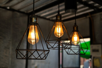 Classic style lightbulb ceiling lamp with iron cage glowing in orange light shade. Interior decoration object photo, selective focus.