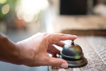 A guest's hand is ringing bell which is placed on the counter desk for calling the restaurant...