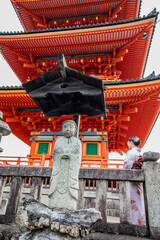 Obraz premium Sublime and famous orange ancient Japanese temple in Kyoto, Japan with unrecognizable Geisha at the foot of the temple, vertical image