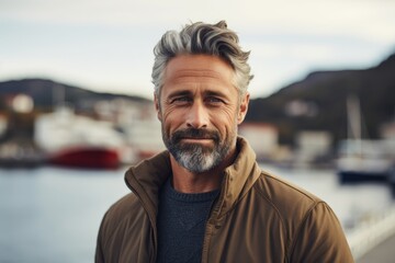 A mature man with grey hair and a beard standing in front of a body of water. Versatile image suitable for various themes