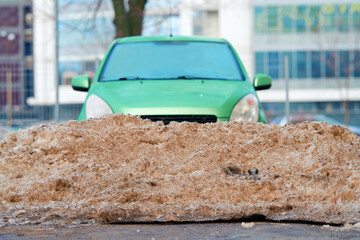 Pile of dirty snow after plowing parking lot. Snowdrift and freezed green car. Сar locked in...