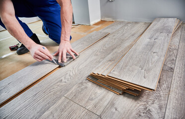 Man preparing laminate plank for floor installation in apartment under renovation. Close up of male...