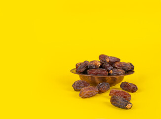 Dry dates fruits, side view close up image of copper bowl dry dates fruits. Yellow studio background, copy space. Ready to eat for Iftar time. Islamic religious ramadan month concept idea.