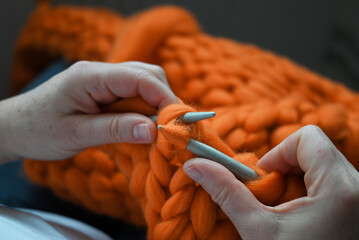 Women's hands knit traditional orange wool products with large needles. Part of knitting woolen products