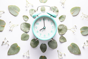 Retro style blue alarm clock with fresh eucalyptus leaves and flowers on white background top view.