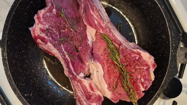 Big red beef stake on a black pan with rosemary ready for cooking, black pepper on top