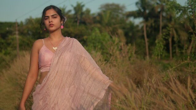 Woman in traditional saree walking through a field at sunset, reflective mood