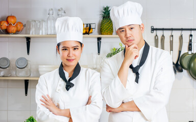 Asian smart couple male female chef wearing white uniform, smiling with happiness, preparing for cooking in kitchen, looking at camera. Restaurant, hotel, Food Concept.