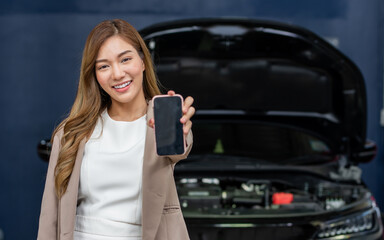 Portrait adult beautiful Asian female customer smiling, satisfied, positive evaluation with car maintenance service, showing, holding, using mobile phone for payment. Service, Industry Concept.