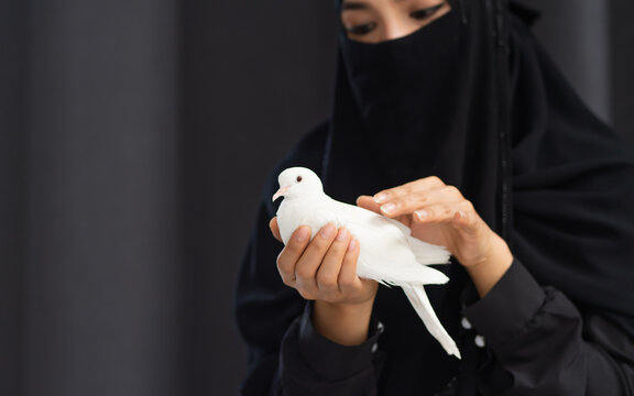 Portrait with copy space adult beautiful Muslim woman wearing black headscarf, traditional dress, smiling with happiness, holding white bird, showing freedom, beauty. Diversity, Woman Power Concept.