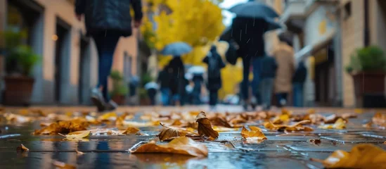 Fotobehang Blur obscures faces as people walk by with rain gear and leaves litter the wet sidewalk of a Udine alley on a rainy autumn day. © Emin