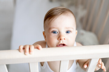 close-up portrait of a little baby girl in a crib, a cunning look of a baby at home in a nursery in...
