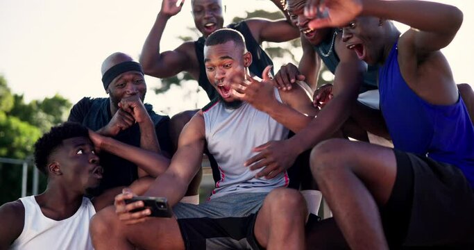 Phone, fitness and sports fans watching game outdoor on basketball court for celebration or reaction. Exercise, support and social media with athlete team on bleachers together for mobile streaming